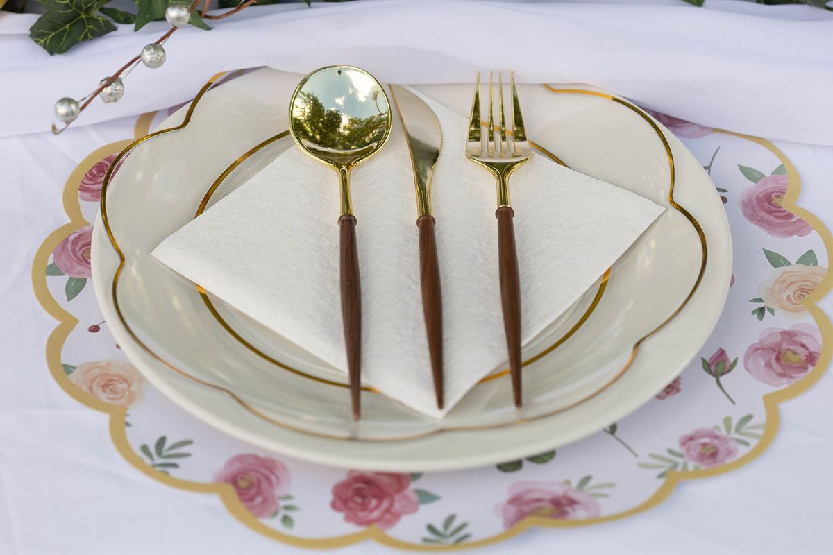 Place setting with a floral-rimmed charger, white folded napkin, and gold-handled flatware